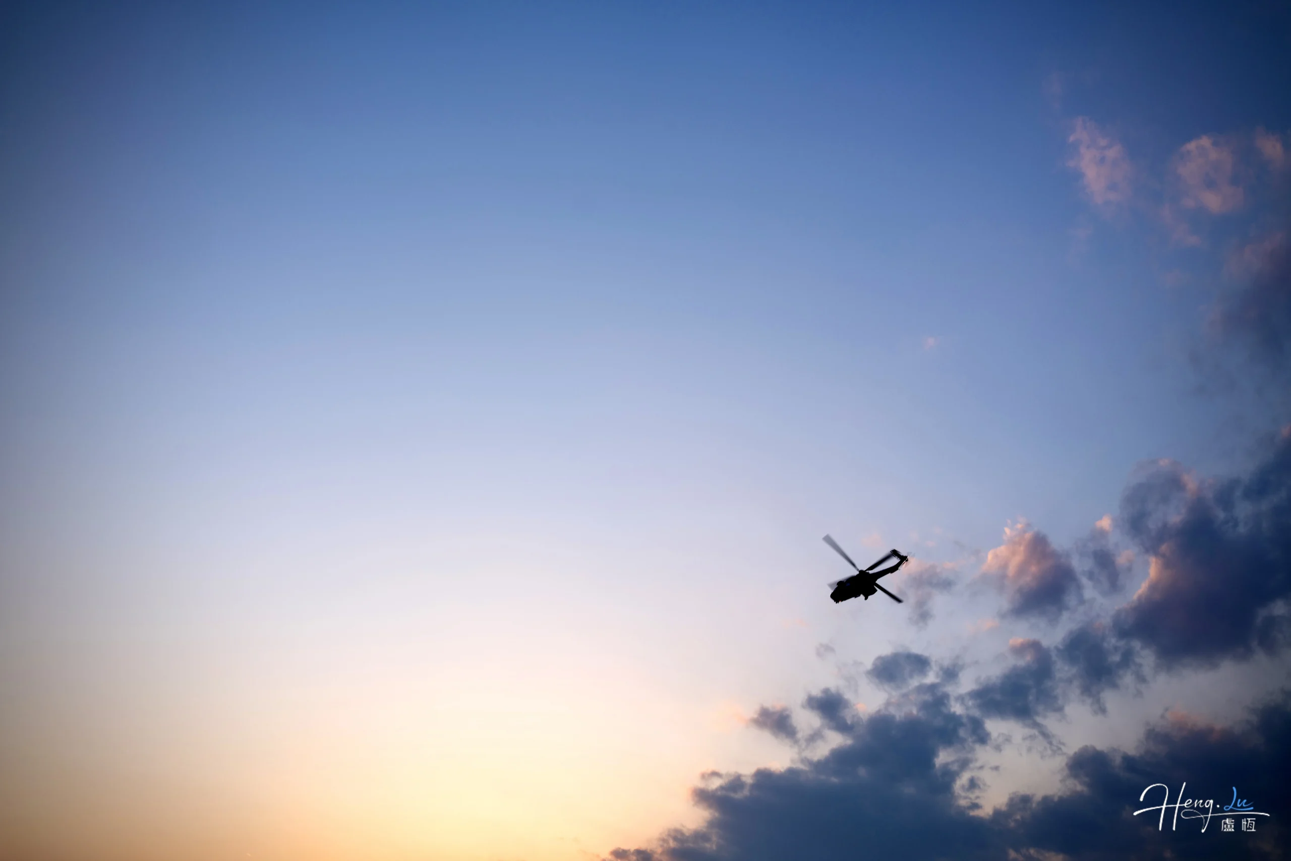 Silhouette d’un hélicoptère dans un ciel bleu pâle et orangé au crépuscule