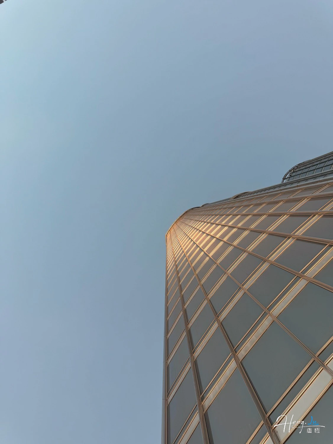 A curved tower catches golden light against a pale blue sky.