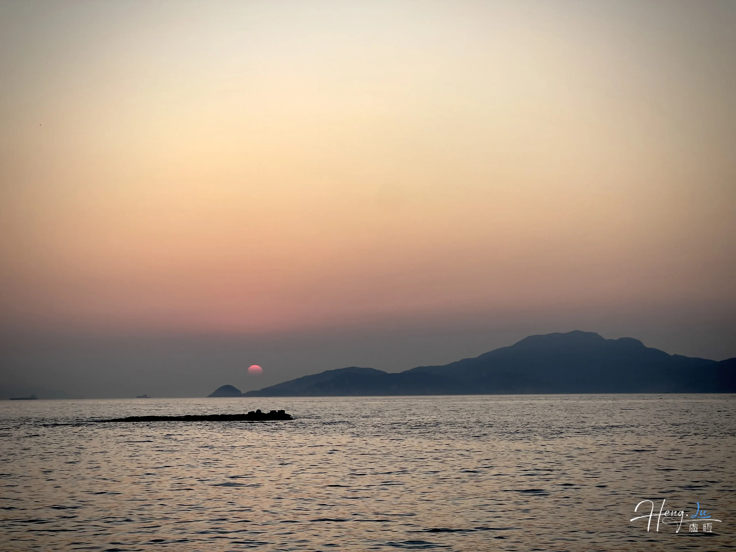 Una tranquila puesta de sol sobre el mar en calma, con sombras lejanas que cubren las montañas.