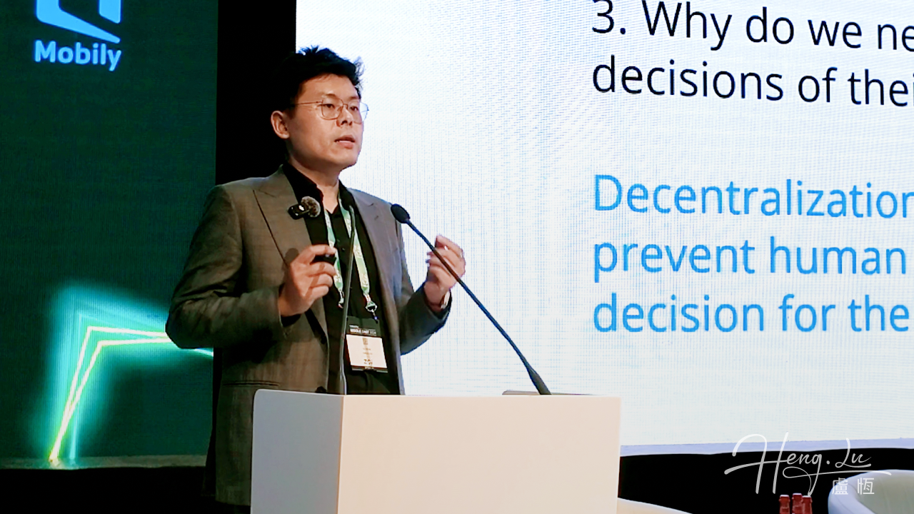 Lu Heng speaking at a lectern in front of a presentation about decentralization.