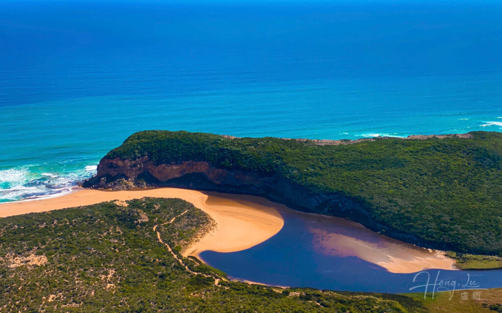Coastal lagoon with sandy beach and green cliff next to ocean