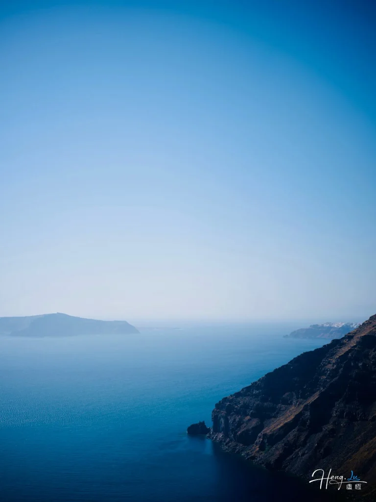 Clear Blue Sea and Rocky Coastline Under Bright Sky with Distant Island Clear-blue-sea-with-rocky-coastline