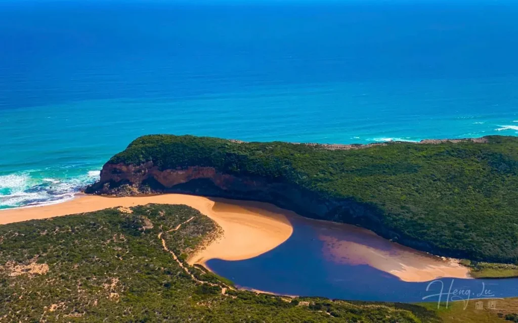 Coastal lagoon with sandy beach and green cliff next to ocean Lagoon-and-ocean-coastline