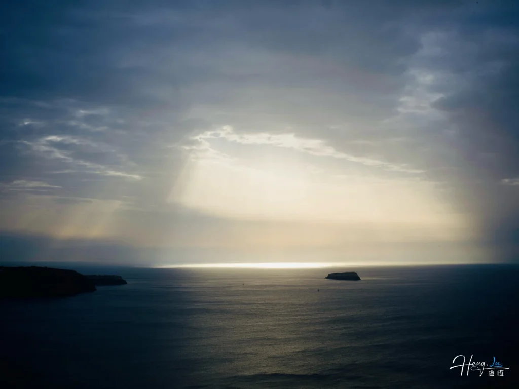 Sunlight Rays Breaking Through Clouds Over Calm Ocean Horizon with Island Sunlight-rays-over-calm-ocean-horizon